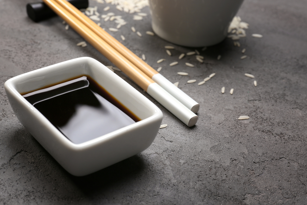 Bowl with tasty soy sauce on grey textured background