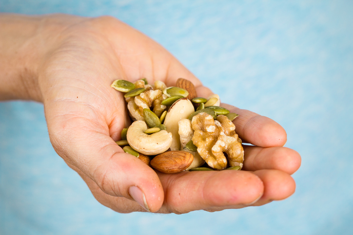 A hand holding a wide variety of nuts and seeds.