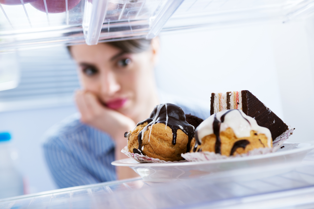 Young hungry woman in front of refrigerator craving chocolate pastries.